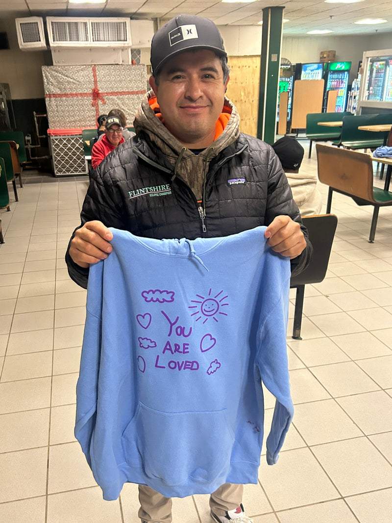 Person holding a blue sweatshirt with text in an indoor setting