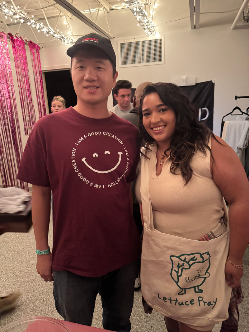 Two people standing together, one wearing a cross body bag that says "Lettuce Pray"